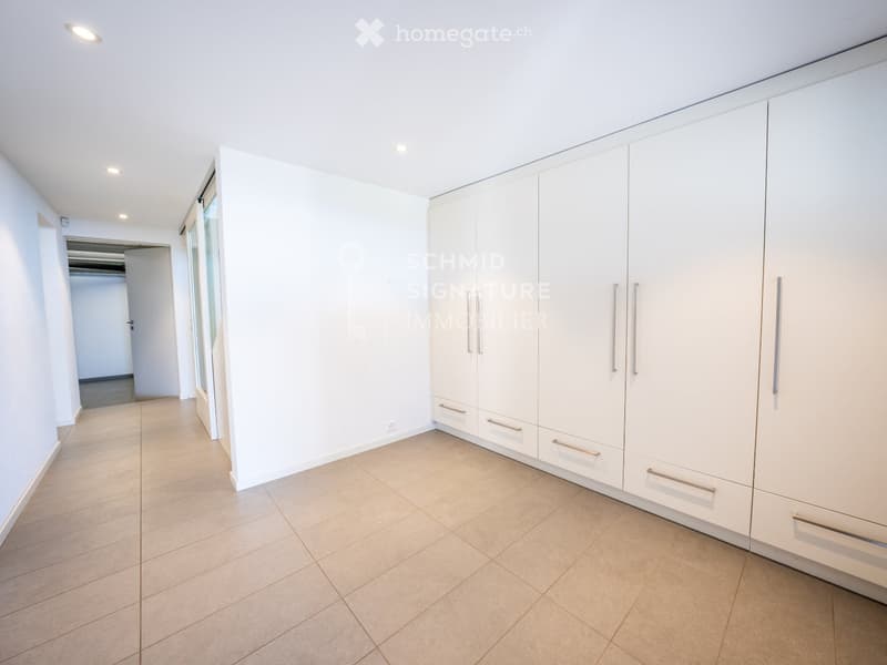 Empty hallway with white walls, tiled floor, built-in white closet with silver handles, and recessed lighting.
