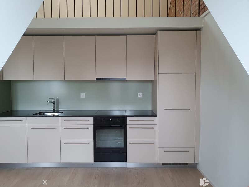 Modern kitchen with light-colored cabinets, stainless steel sink, and built-in oven. The space features a sleek, contemporary design with a wooden floor and minimalist aesthetic.