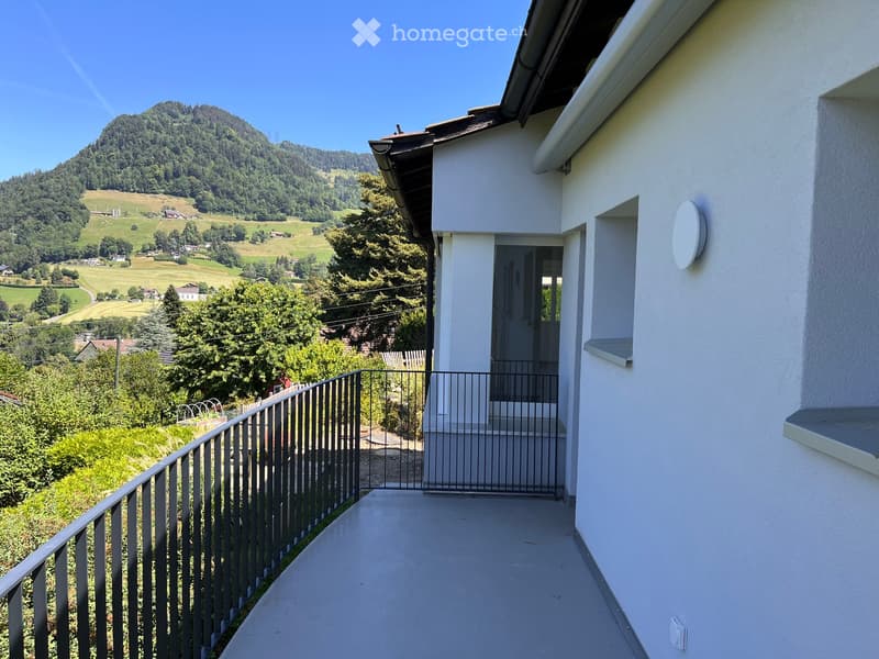 Balcony with metal railing, overlooking a green landscape and distant hills.