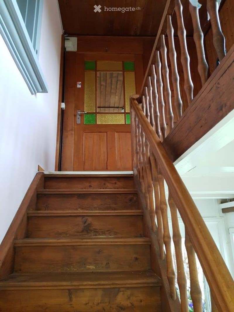 Wooden staircase with a handrail and a wooden door at the end, featuring a stained glass panel.