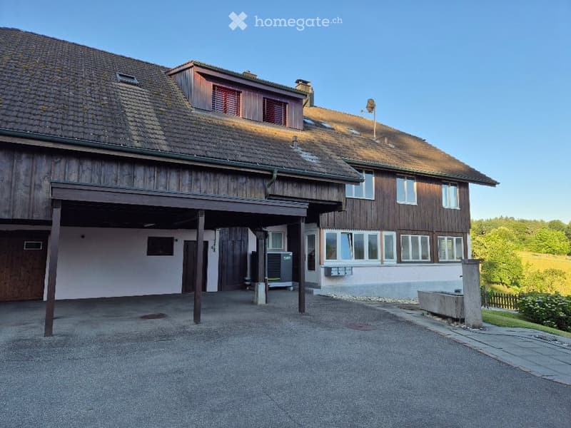 Two-story wooden house with a tiled roof, large garage, and multiple windows. The building features a mix of wood and plaster finishes.