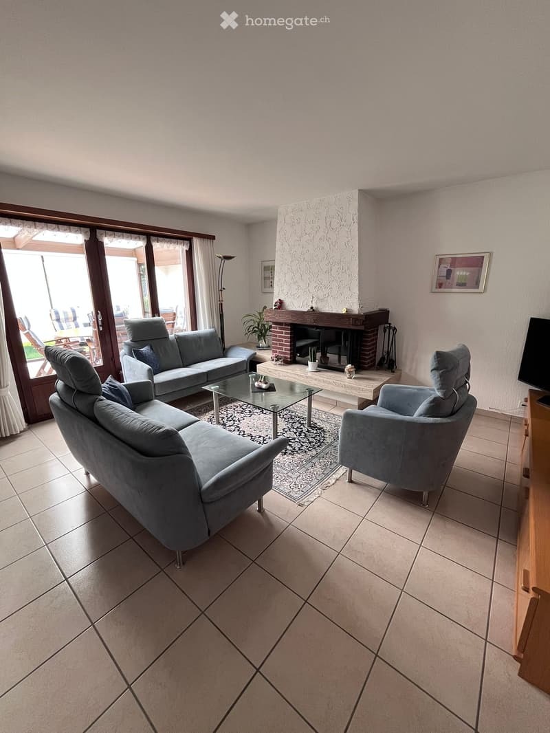 Modern living room with tiled floor, fireplace, grey sofa, coffee table, armchair, and television.