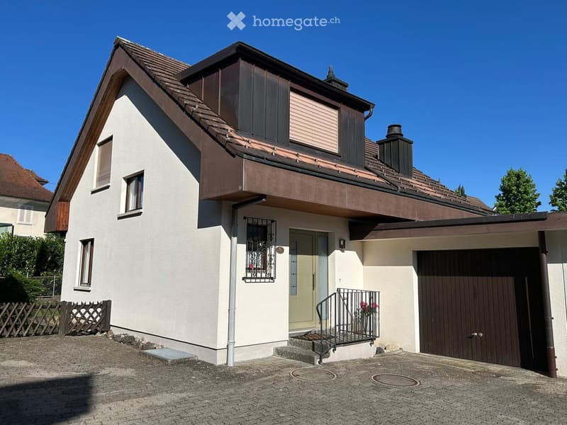Two-story house with a modern design, featuring a garage, a small balcony, and a staircase leading to the entrance.