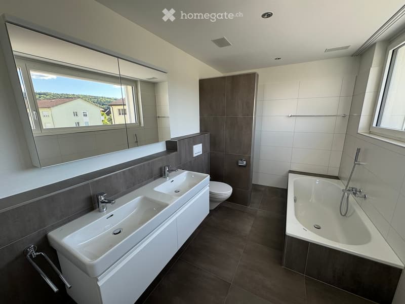 Modern bathroom with double sink, bathtub, toilet, large mirror, and large windows offering a view of the landscape.