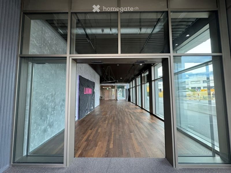 Modern hallway with wooden flooring, large glass windows, and a visible sign on the wall.