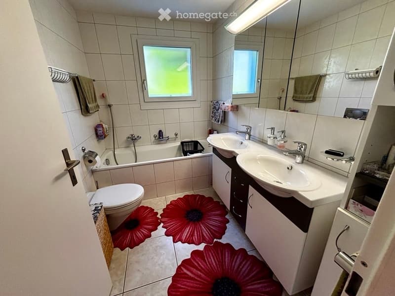Bathroom with a toilet, bathtub, double sink, mirror, and red flower rugs on the floor.