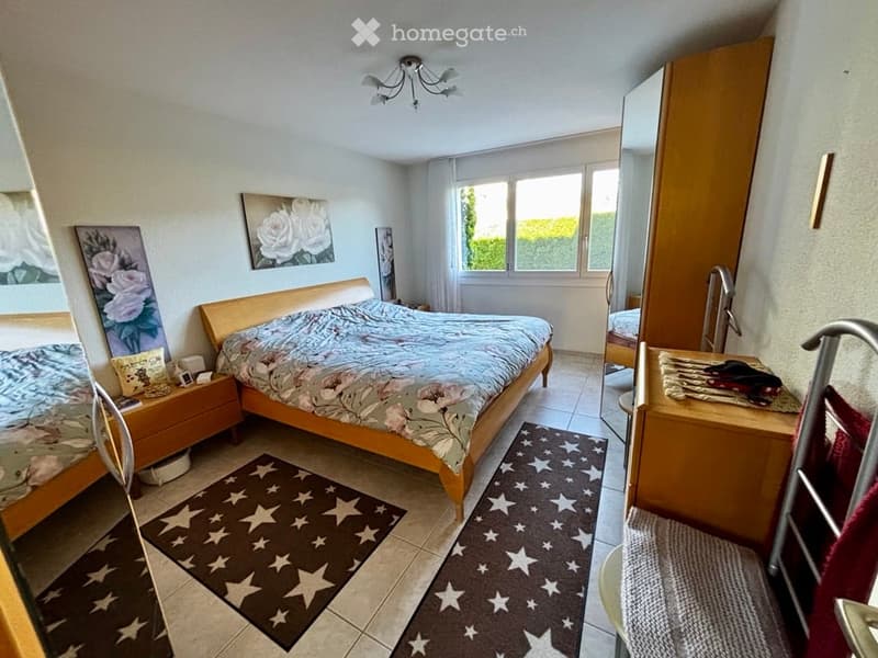 Cozy bedroom with a double bed, nightstand, mirror, wardrobe, and artwork on the walls. The room features tiled flooring and two star-patterned rugs.