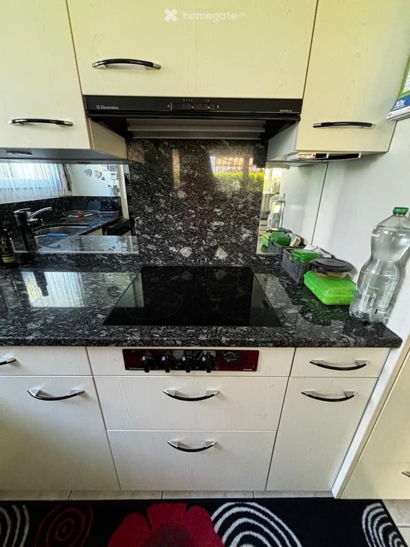 Modern kitchen with white cabinets, granite countertops, a built-in stove, and a sink. A bottle and a green container are on the counter.