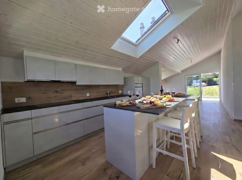 Modern kitchen with white cabinets, wooden accents, island, and stools, featuring a skylight and a view of the garden.