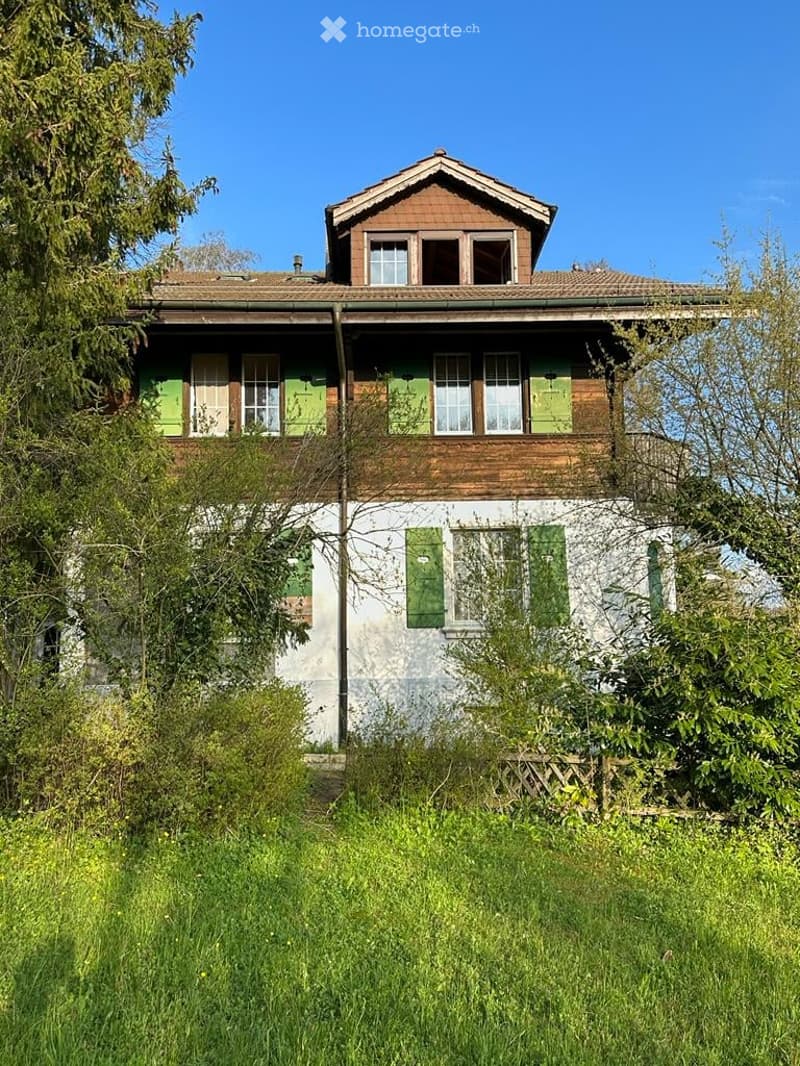 2 story house, brown roof, green shutters, white and brown walls, surrounded by trees and grass