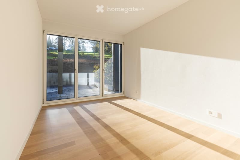 Empty room with white walls, wooden floor, and large sliding glass doors leading to a terrace.