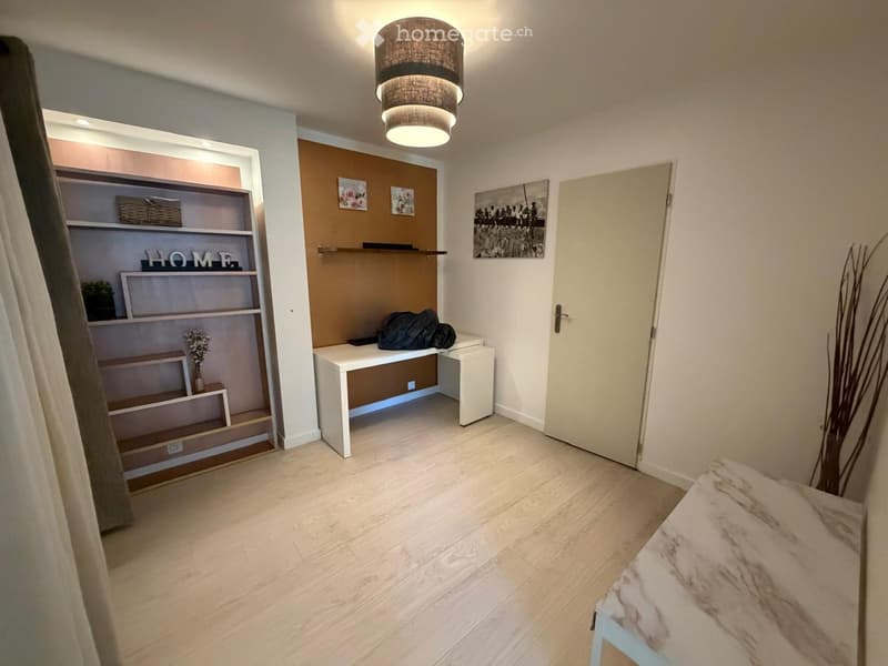 Modern, minimalist bedroom with light wooden flooring, white desk, built-in shelving unit, decorative picture frames, and a small vase with flowers.