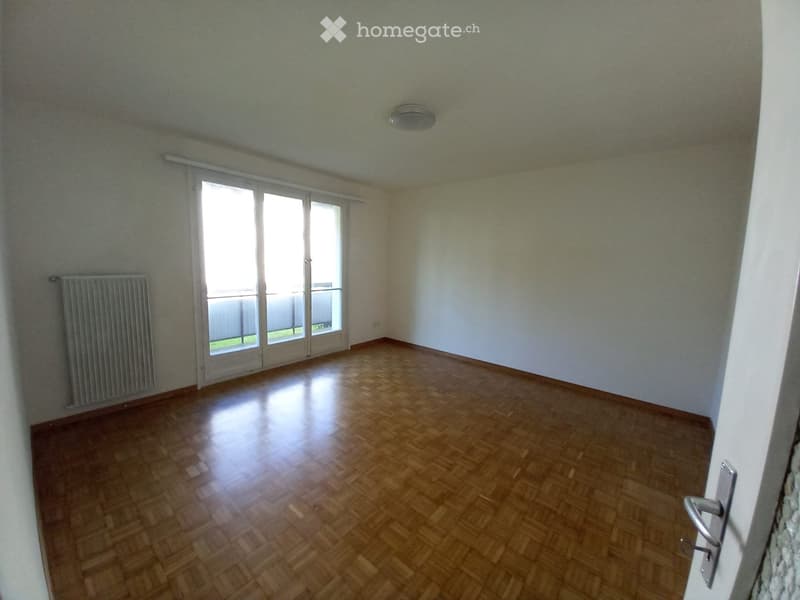 Empty room with wooden flooring, white walls, large sliding glass door leading to a balcony, and a radiator on one wall.