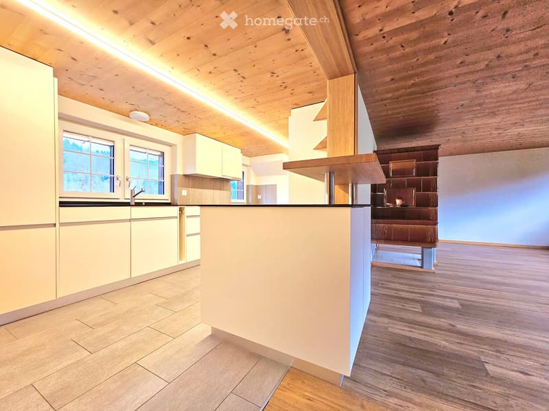 Modern kitchen with light-colored cabinets, a central island, and a sleek countertop. The space features wooden flooring and a cozy fireplace area visible in the background.