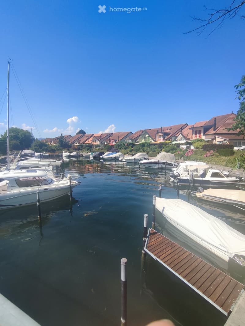 A serene marina with several docked boats, surrounded by residential houses with red-tiled roofs and lush greenery.