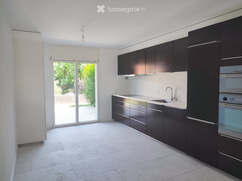 Modern kitchen with dark cabinets, white countertops, and a built-in oven. Features a large window with a view of greenery outside.