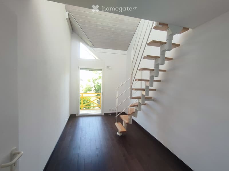 Modern hallway with dark wooden flooring, white walls, and a spiral staircase leading upwards. Features a glass door with a yellow frame leading outside.