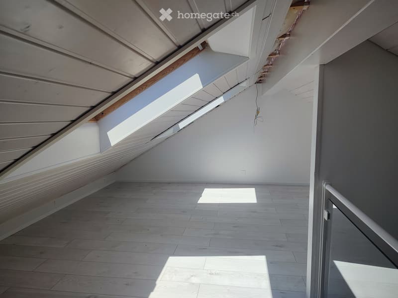 Empty attic space with wooden flooring, white walls, exposed wooden beams, and skylight windows allowing natural light.
