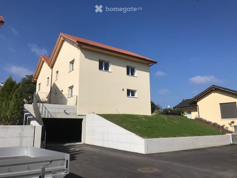 Two-story house with a raised ground floor, garage, and a small landscaped garden area.