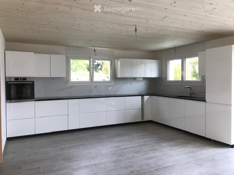Modern, minimalist kitchen with white cabinets, a central island, and grey countertops. Features include an integrated oven and a sink with a modern faucet.