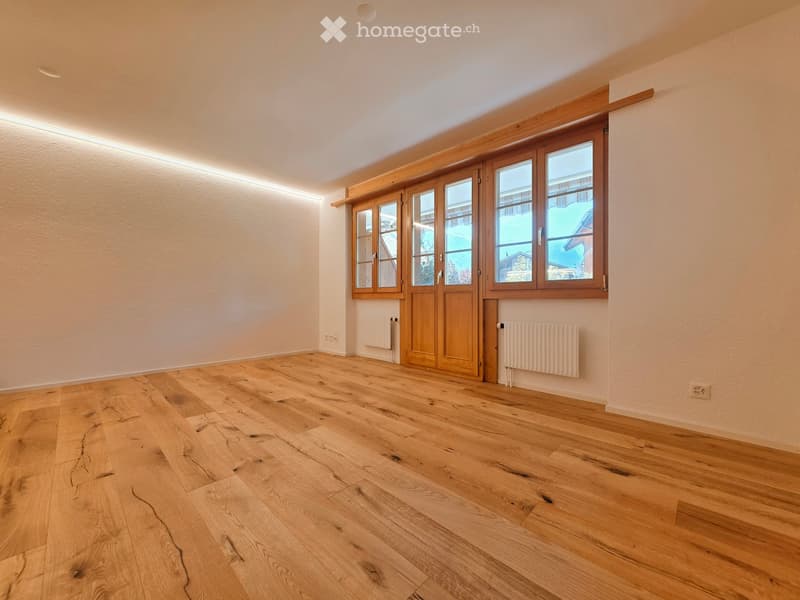 Empty room with wooden flooring, large windows, and radiators on the walls.