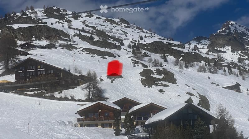 A snowy mountain landscape with several houses and a ski slope, featuring a ski lift and a red overlay on the slope.