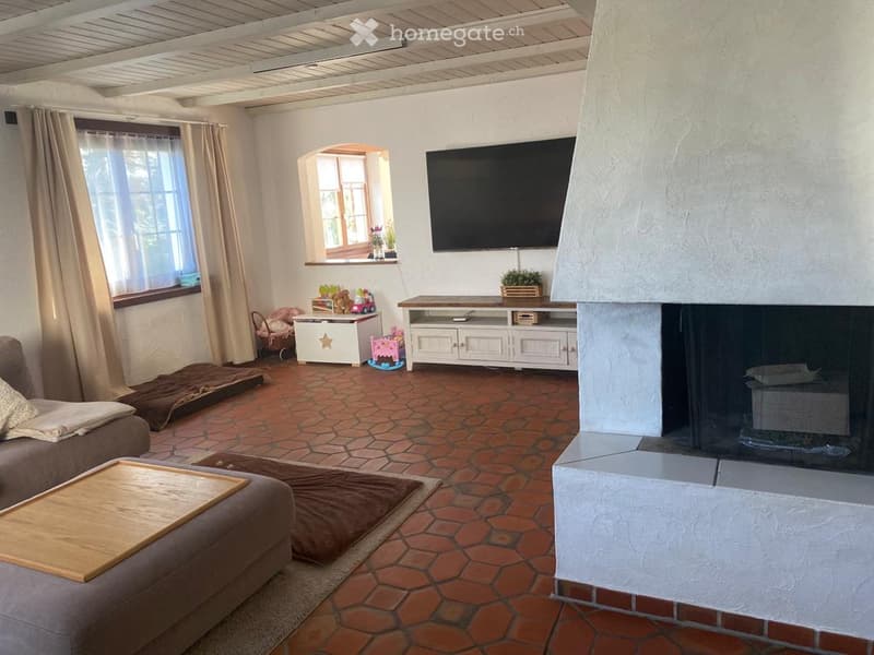 Living room with a fireplace, TV, sofa, coffee table, and cabinet. The room features a tiled floor and large windows with curtains.