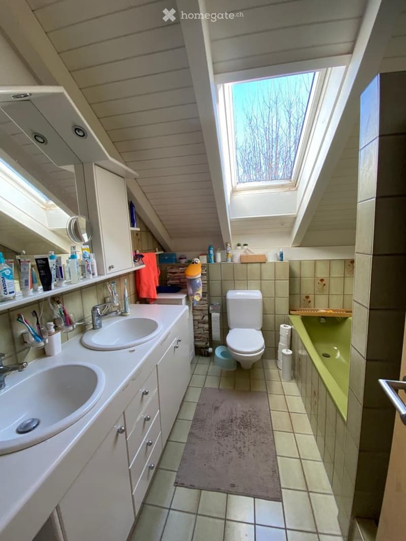 Bathroom with two sinks, a toilet, a bathtub, and a skylight window. The room features wooden paneling on the ceiling and tiled walls.
