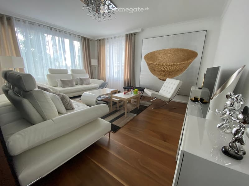 Modern living room with white leather sofas, a coffee table, a small side table, a hanging woven basket, and a decorative sculpture on a console table.