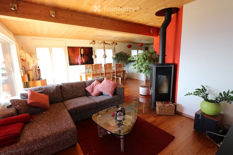 Living Room. Cozy living room with a grey sectional sofa, glass coffee table, fireplace, dining area with chairs and table, and decorative plants.