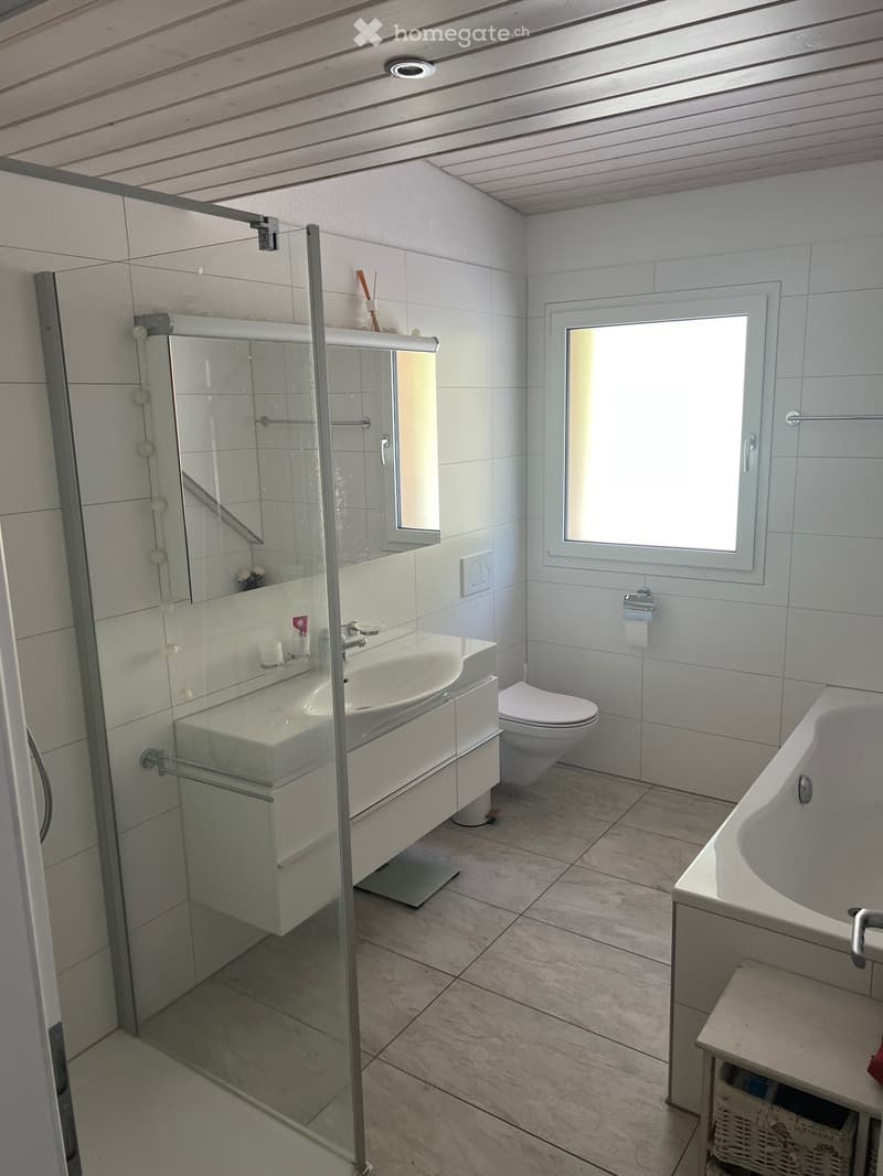 Modern bathroom with white tiles, a large window, a glass-enclosed shower, a sink with a mirror, a toilet, and a bathtub.
