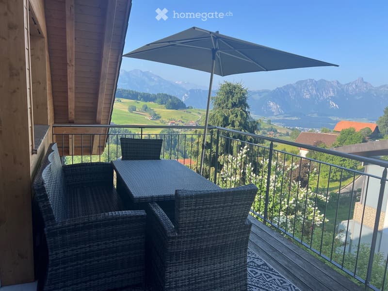 Balcony with wicker furniture, umbrella, and scenic mountain view.