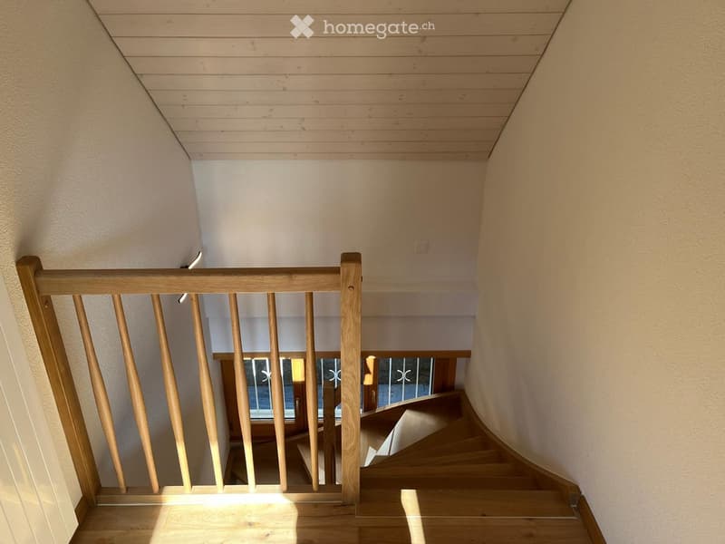 Wooden staircase with a wooden railing and light-colored walls, leading to a lower level with a window and door visible at the bottom.
