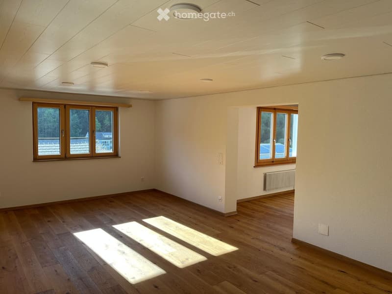 Empty room with wooden flooring, white walls, and large windows allowing natural light to enter. The ceiling features recessed lighting.