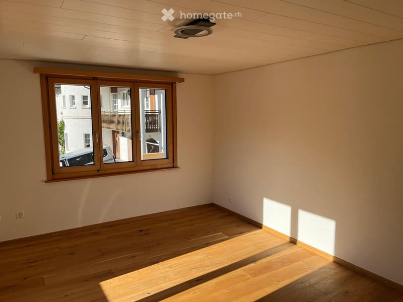 Empty room with wooden flooring and large windows, allowing natural light to fill the space.