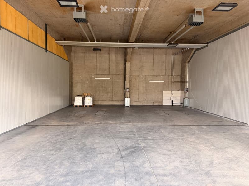Empty garage with concrete walls, grey tiled floor, and minimal fixtures including a sink and storage units.