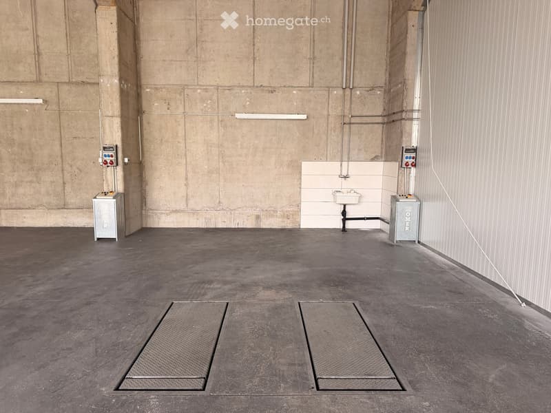 Empty room with concrete walls and floor, two metal grates, a sink, and control panels.