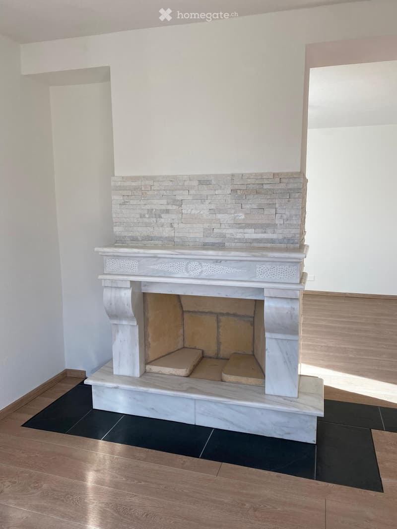 A modern fireplace with a marble surround and decorative stonework, set against white walls and a mix of dark and light flooring.