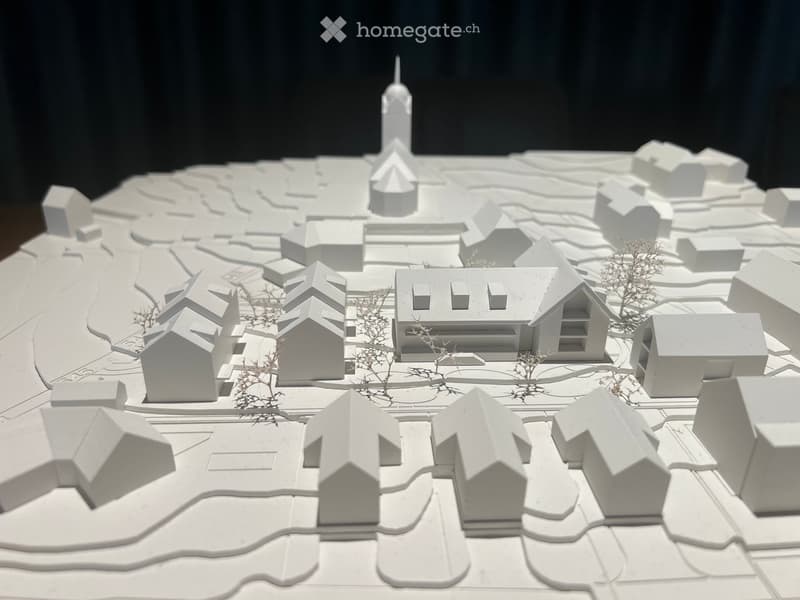 Architectural model of a small town with multiple houses, a church tower, and surrounding landscape.
