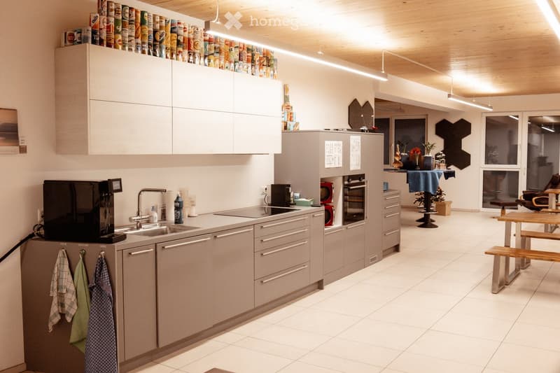 Modern kitchen with white cabinets, stainless steel appliances, and a central island. Includes a refrigerator, sink, oven, microwave, coffee machine, and hanging towels.