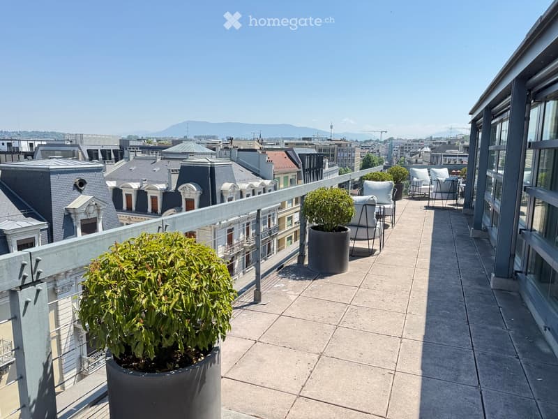A modern rooftop terrace with a cityscape view, featuring two white chairs, a small table, and two large potted plants.