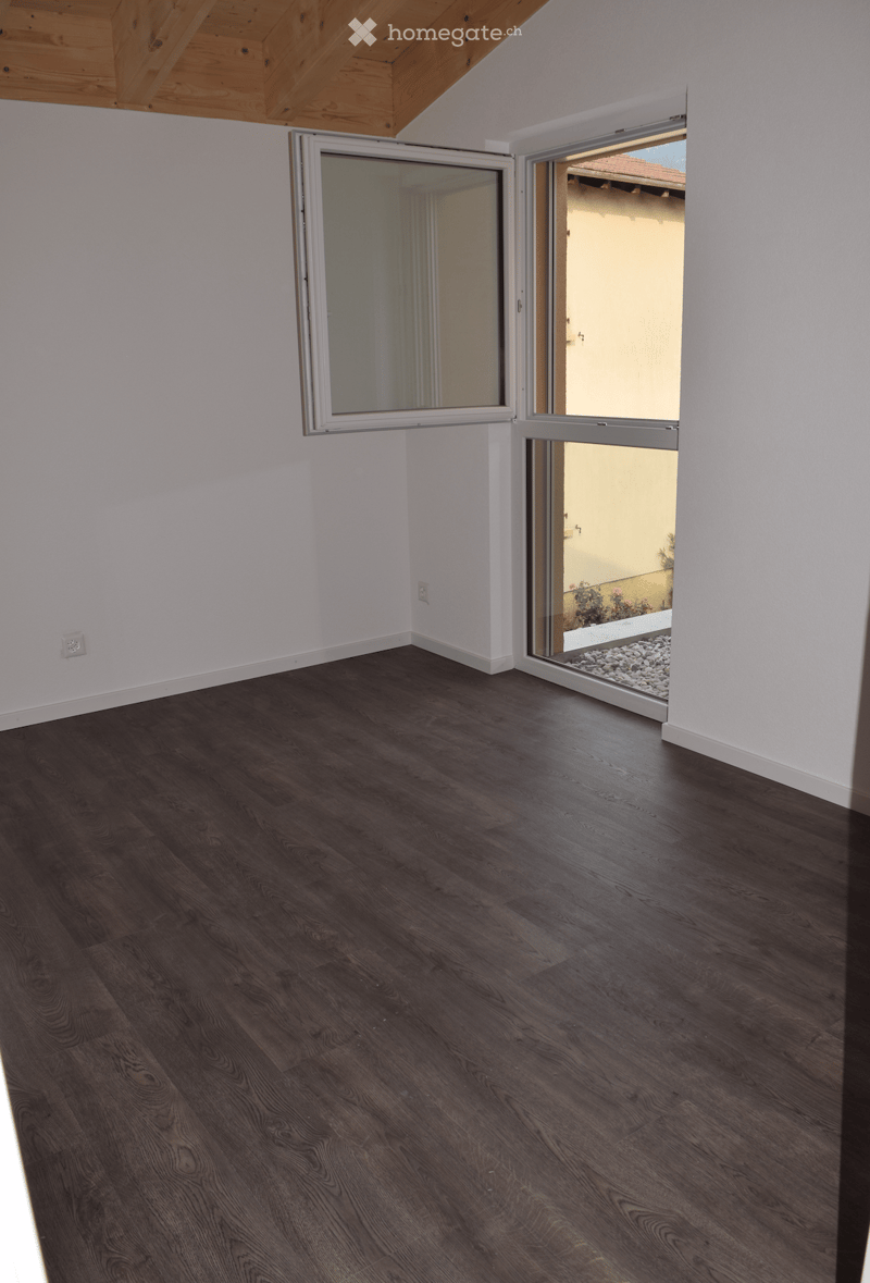 Empty room with dark wooden flooring, white walls, and large sliding glass doors leading to an outdoor area.