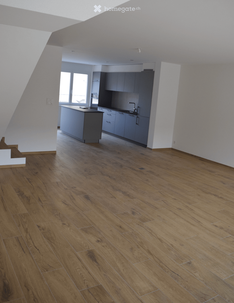 Open-plan space with wooden flooring, white walls, and a modern kitchen area featuring cabinets and a countertop. The room is completely empty with no furniture or personal items.