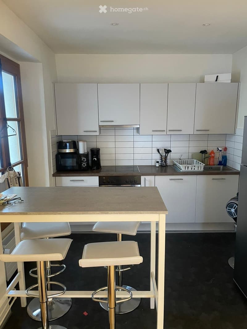 Modern kitchen with white cabinets, stainless steel appliances, and a central island with four white bar stools.
