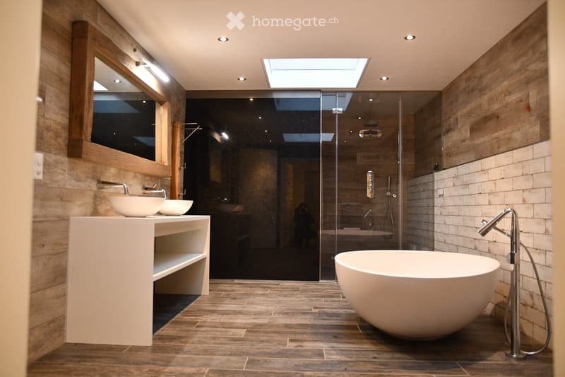 Modern bathroom with wooden walls, a large freestanding bathtub, double sink vanity, and a glass-enclosed shower area with a skylight above.