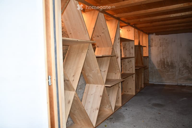 Empty room with exposed wooden beams and geometric wooden shelving units, concrete floor, and unfinished walls.