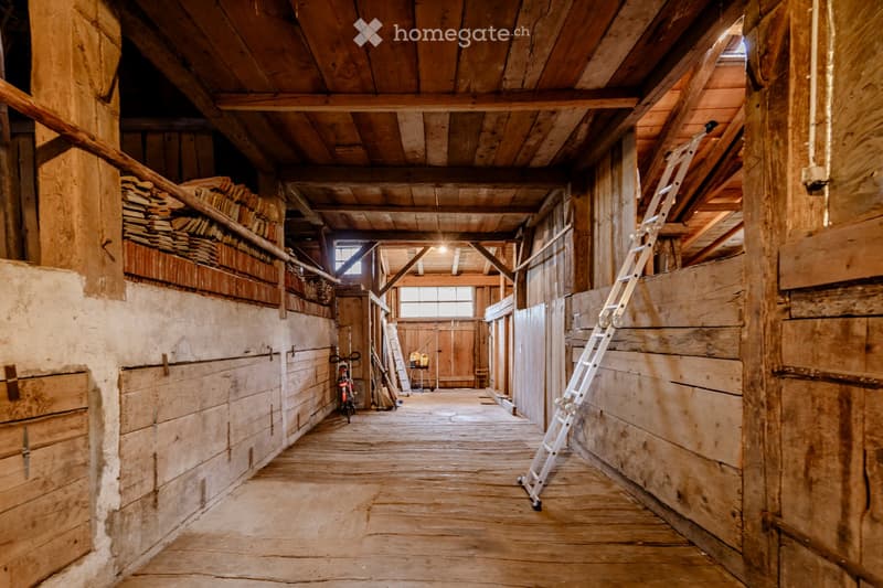 A rustic wooden hallway with exposed wooden beams and plank flooring, featuring ladders, bicycles, and storage shelves along the walls.