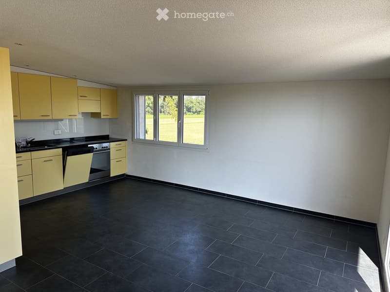 Modern kitchen with yellow cabinets, black tiled floor, and large window overlooking a green area.