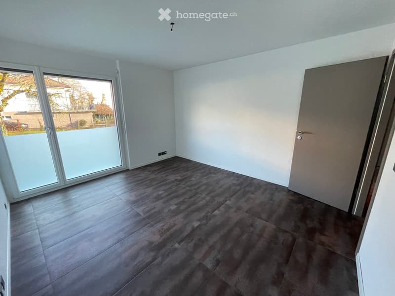 Empty room with dark grey tiled floor, white walls, large sliding glass door leading outside, and a closed door on the right side.