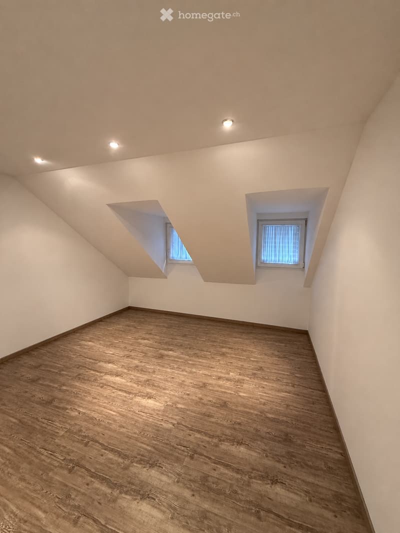 Empty room with wooden flooring and white walls, featuring two small windows and recessed ceiling lights.